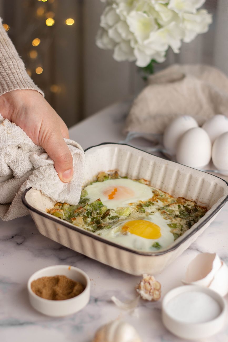 hand of a person placing a dish in a baking pan onto a table
